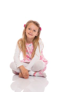 Full length portrait of a little girl with long hair sitting with crossed legs on the floor and smiling. Isolated on white background.