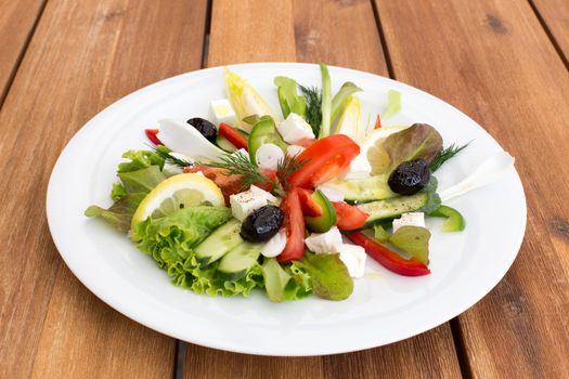 Greek salad with feta, tomatoes, cucumber, peppers and black olives on a wooden table.