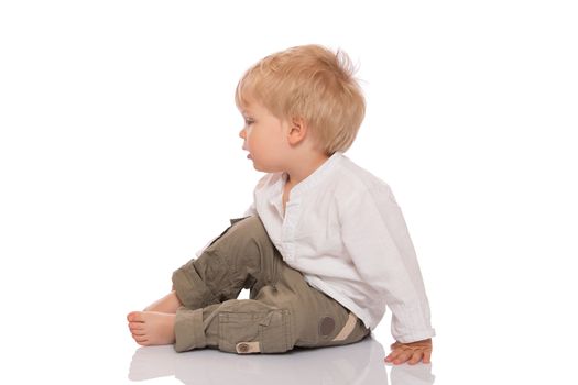 Little child with blond hair sitting on the floor and looking at something. Isolated on white background.