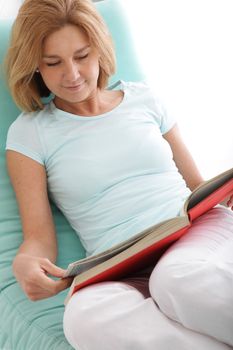 Fresh woman lying on the couch and reading book indoors