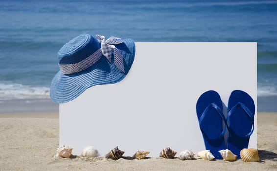 White board with flip-flops, hat and seashells on sandy beach 