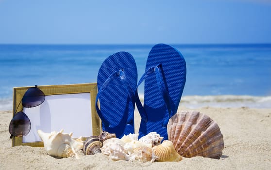 Flip-flops with photoframe, sunglasses and seashells on sandy beach