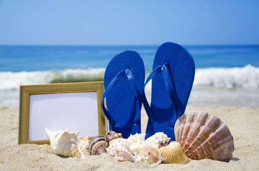 Flip-flops with photoframe and seashells on sandy beach