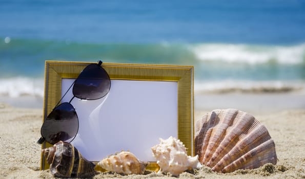 Photoframe with seashells and sunglasses on sandy beach