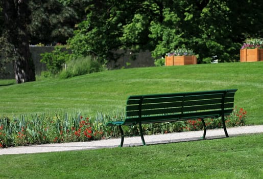 Back of a green bench in front of a small way, flowers and green grass