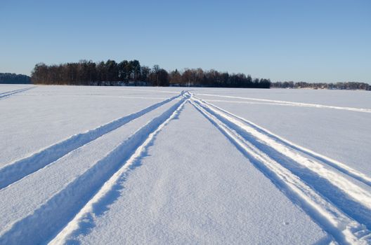 Snowmobile winter transport wheel marks left on frozen lake snow.