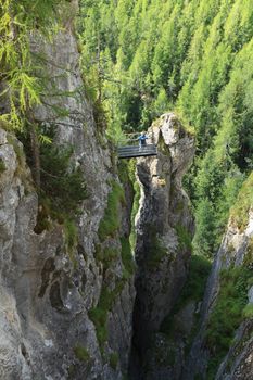 woman on via ferrata Sass de rocia with a metal bridge on top of a monolith, Italian Dolomites