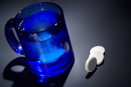 Vitamin C tablet dissolving in a blue glass of water.