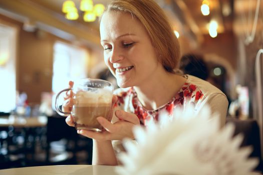 Portrait of girl enjoying coffee latte in cafe. Beautiful vintage interior in blur with natural sunlight.