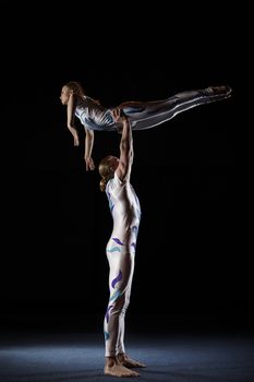 Circus artists perform different tricks. Man holding woman.