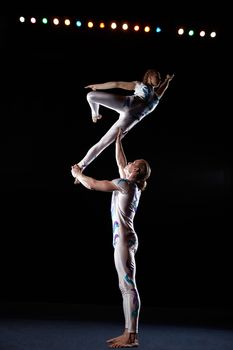 Circus artists perform different tricks. Man holding woman.