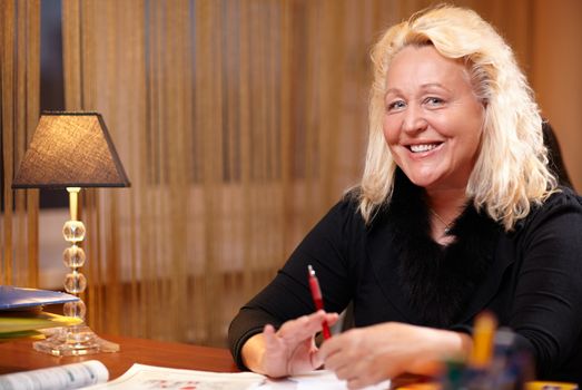 English teacher sitting at the table and smiling to the camera.