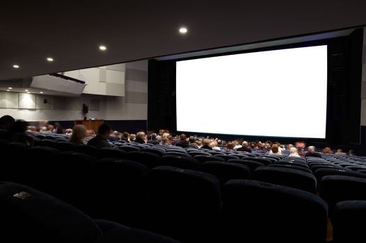 Cinema auditorium with people in chairs watching movie. Ready for adding your own picture. Diagonal perspective view.