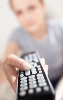 Young woman with remote watching TV. Shallow dof close-up focused on remote control.