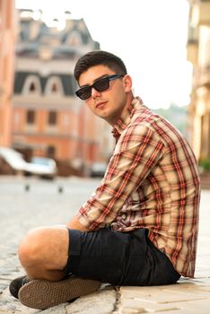 Young handsome man in sunglasses sitting on street