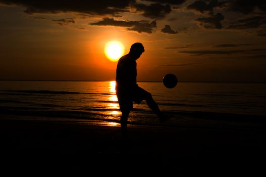 silhouette man playing soccer on the beach