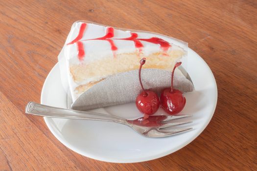 Vanilla cake with cherry on wood background