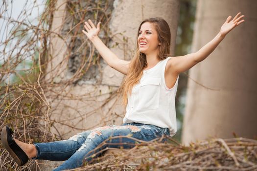 Beautiful caucasian woman in casual sitting next to the old vine with open hands