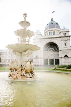 Wealth and real estate with an ornamental white marble fountain cascading into the pond below in front of an arched entrance to a majestic building with a cupola