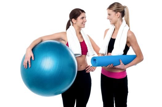 Two girls communicating holding exercise ball and mat