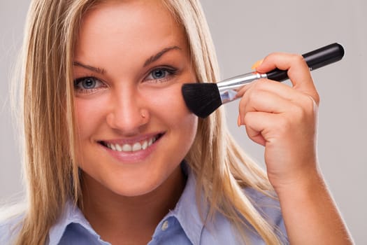 Closeup portrait of young blond caucasian woman smiling with cosmetic brush