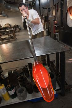 Latino artist blowing into tube with molten glass object