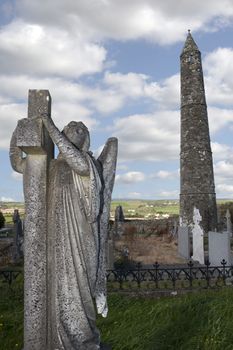 Angel statue before an Ancient round tower and celtic graveyard with cathedral in Ardmore county Waterford, Ireland