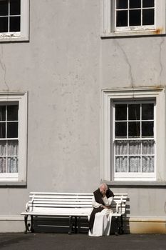 alone monk seated on bench in quiet meditation with Abbey building in background