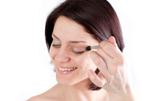 Closeup portrait of a happy young woman applying make up on her face 