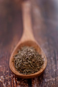 rosemary spice in wooden spoon over wood background - selective focus