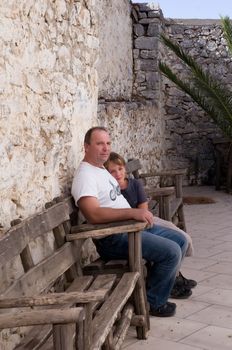 Dad and son sitting on a bench in the courtyard of an old monastery.