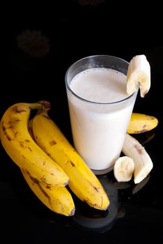 fresh banana smoothie and fruits on black background