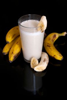 fresh banana smoothie and fruits on black background