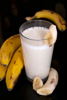 fresh banana smoothie and fruits on black background