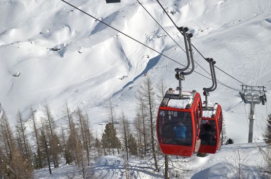 Two red cablecars climbing snow covered mountain, seen from above