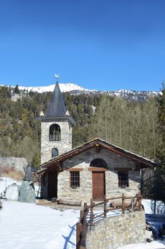 Small, rural chapel in the mountains made of stone. Snow on front yard