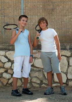 Two young male friends with rackets on tennis court smiling .