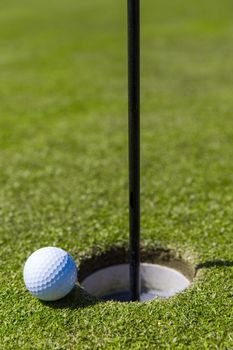 Close up of a golf ball on the edge of a hole.