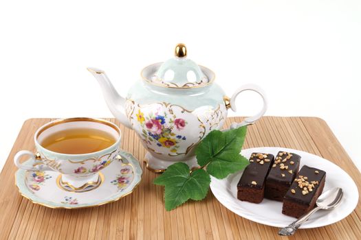 Teapot and cup of tea with 3 brownies on white background