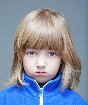 portrait of a boy with long blond hair in blue top - isolated on gray