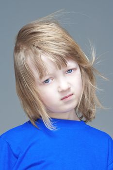 portrait of a sad boy with long blond hair in blue top - isolated on gray