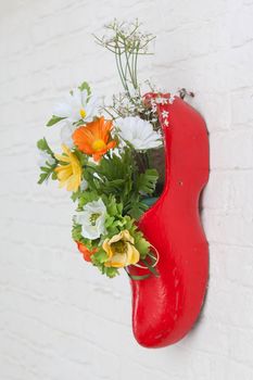 Dutch wooden shoe with fake flowers hanging on a white wall