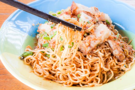 Chopstick holding yellow noodles from spicy noodles