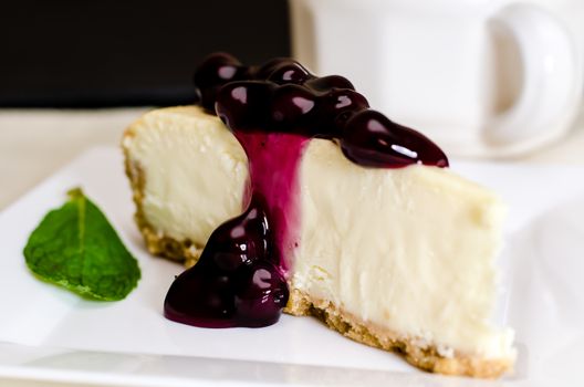 Slice of blueberry cheesecake and coffee with mint garnish.  Shallow depth of field.