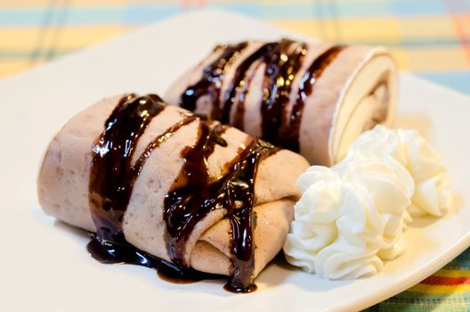 chocolate  crepe rolls  topping with chocolate  syrup served with whipping cream 