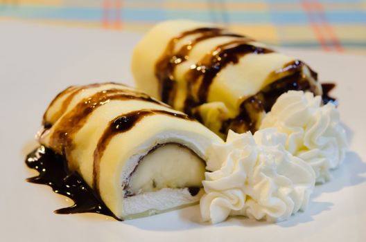 banana crepe rolls filled  with white cream and banana,   topping with chocolate  syrup served with whipping cream