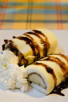 close up crepe rolls filled  with white cream and banana,   topping with chocolate  syrup served with whipping cream