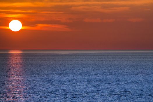 Setting sun with orange sky and blue ocean.