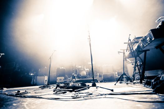 Empty illuminated stage with drumkit, guitar and microphones