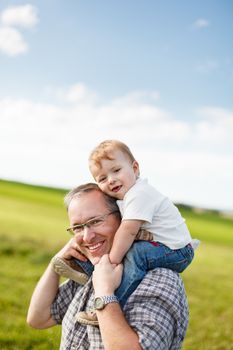 Boy riding his father's shoulders in a field